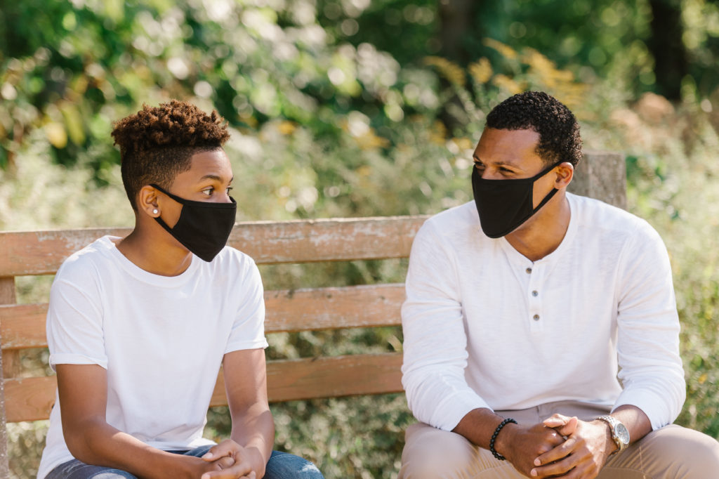 A Little Brother and Big Brother sit masked at a public park